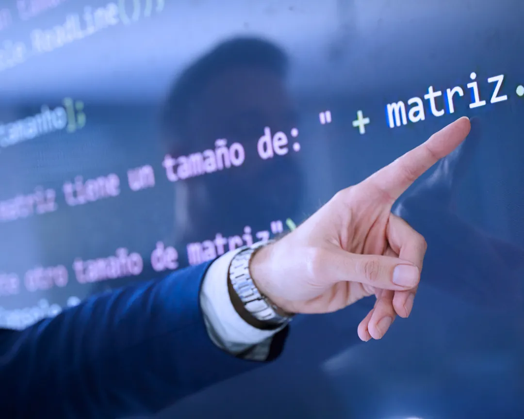 Mano señalando código en una pantalla en una clase de informática de Fomento FP